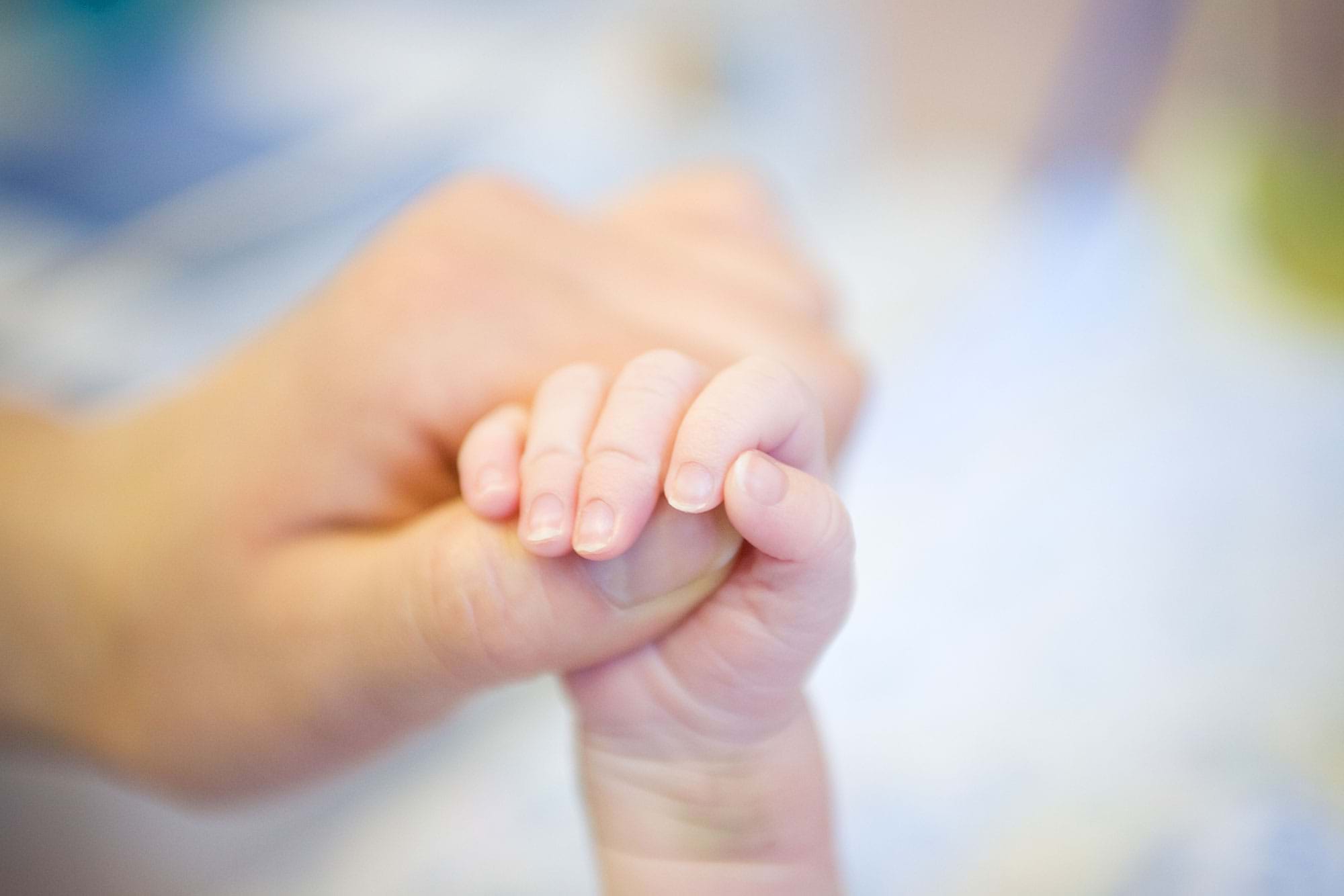 Mother holding newborn baby's hand.